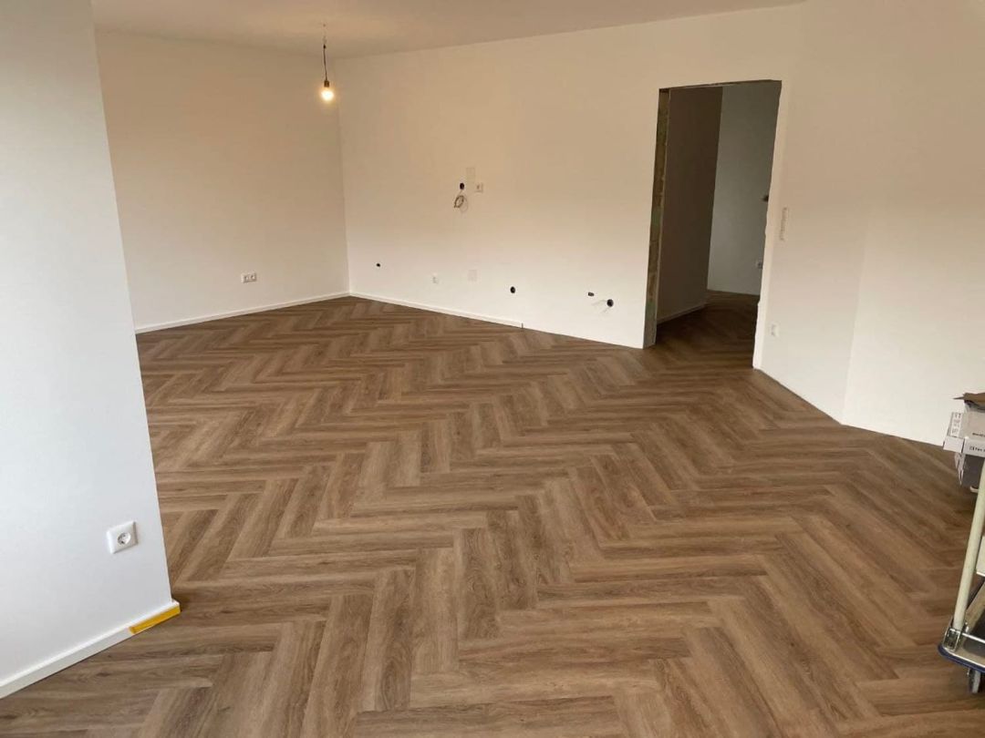Leerer Wohnraum mit im Fischgrätmuster verlegtem Designbelag in Eichenoptik